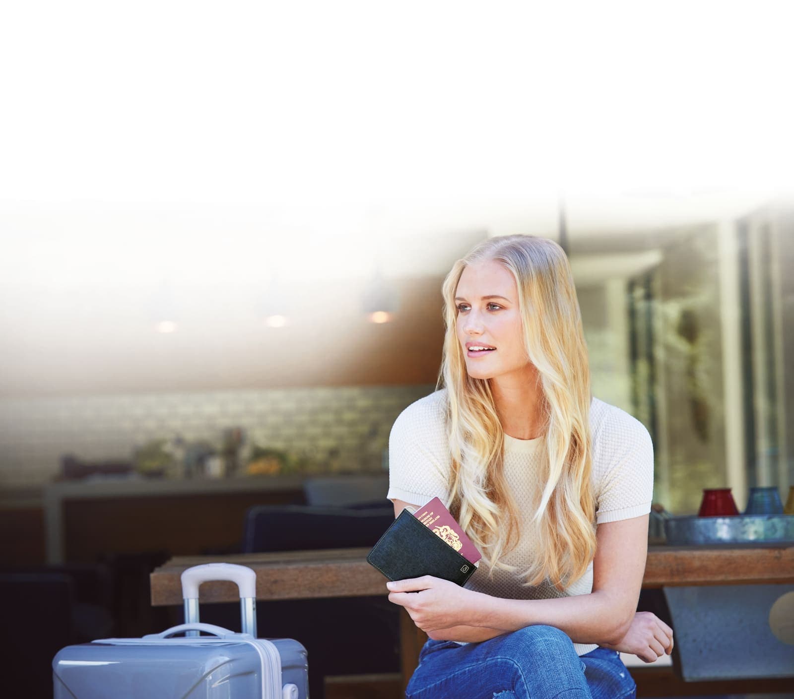 Woman holding passport and boarding pass, with suitcase nearby, ready for travel.