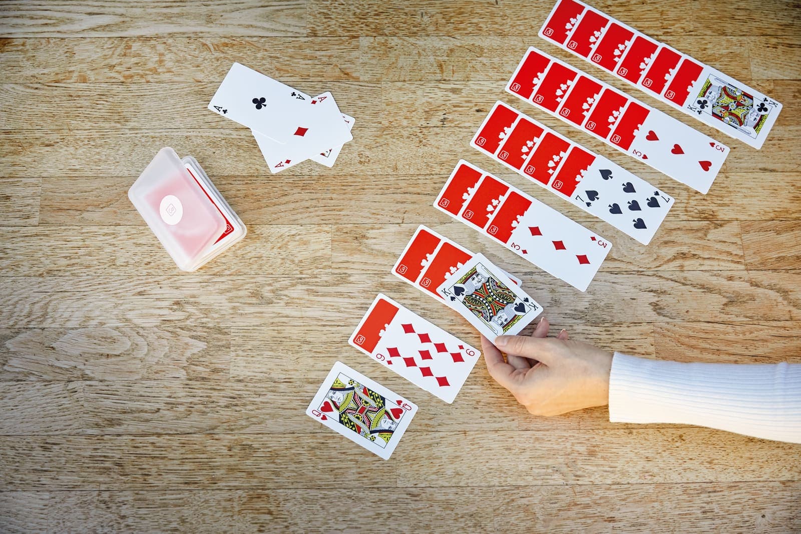 GO TRAVEL waterproof playing cards spread out on a wooden table, with a hand reaching for a card.