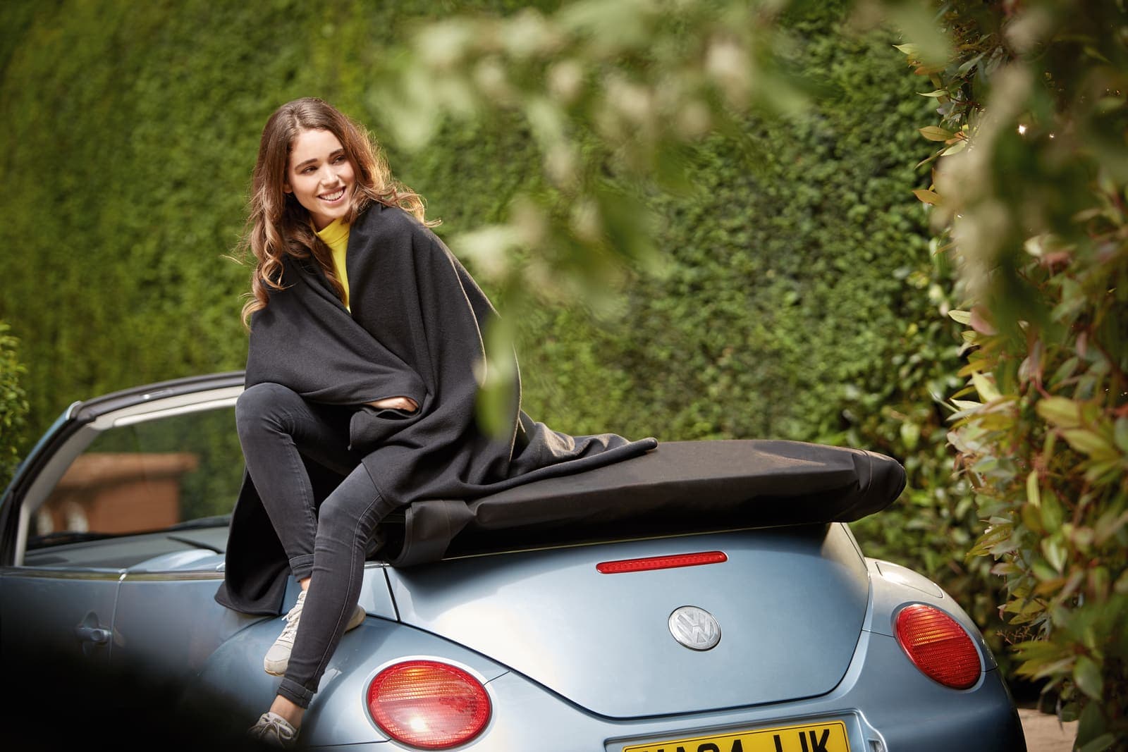 Woman in black blanket sitting on a blue convertible car outdoors.