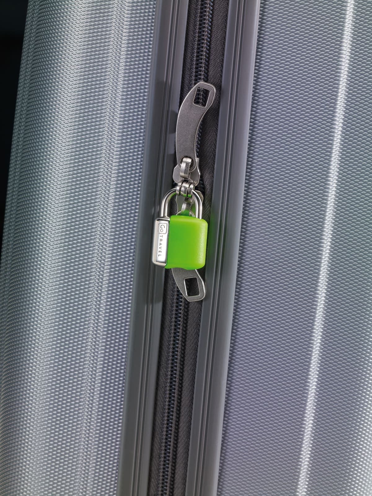 Green GO TRAVEL padlock on a grey suitcase zipper.