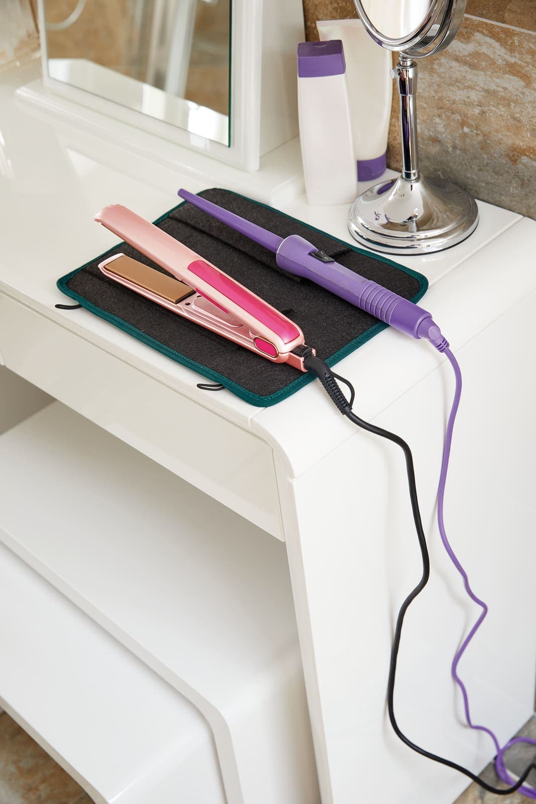 Rose gold hair straightener and purple curling wand on a heat-proof mat.