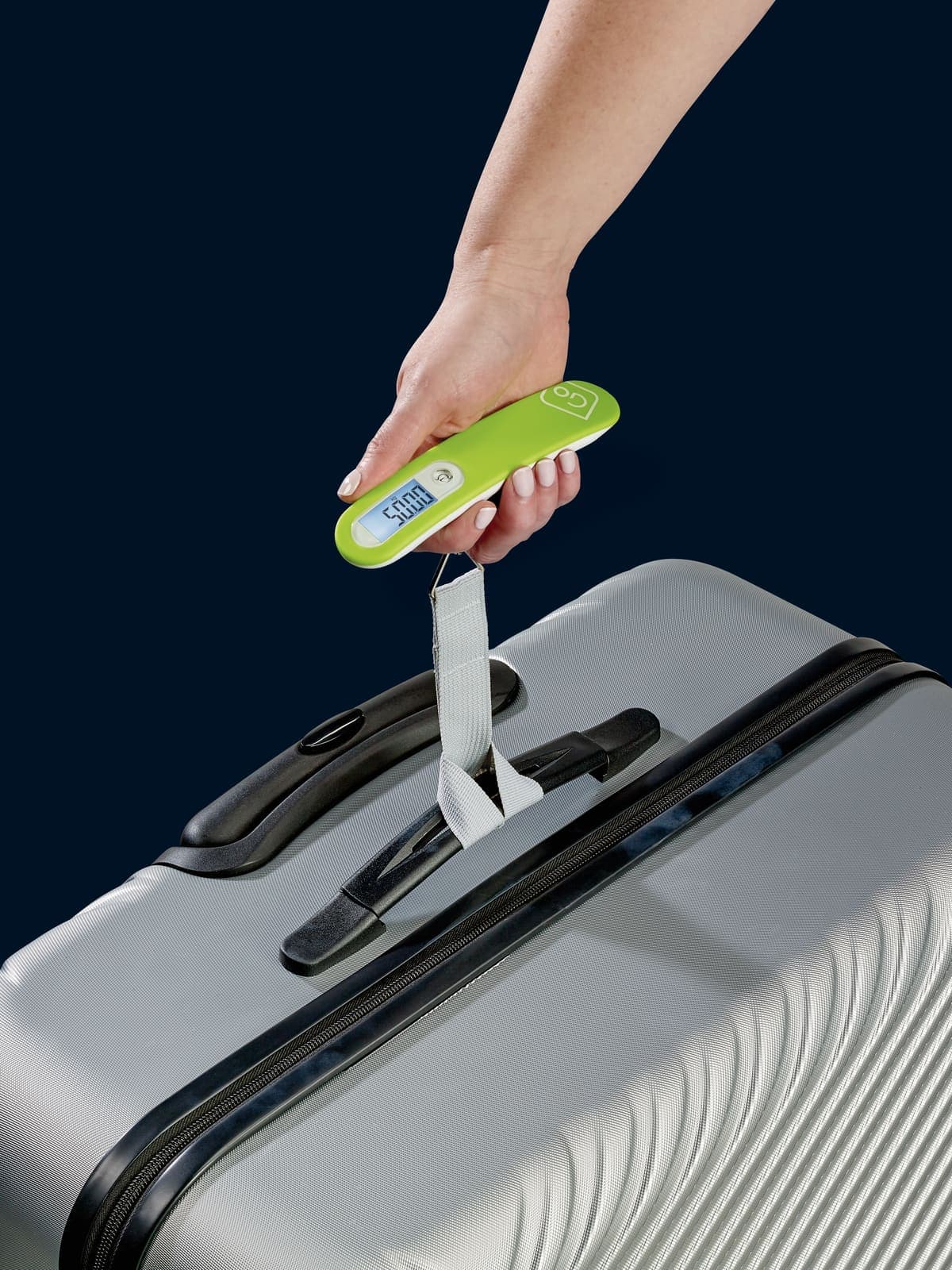 Hand holding a lime green GO TRAVEL digital scale to weigh a grey suitcase.