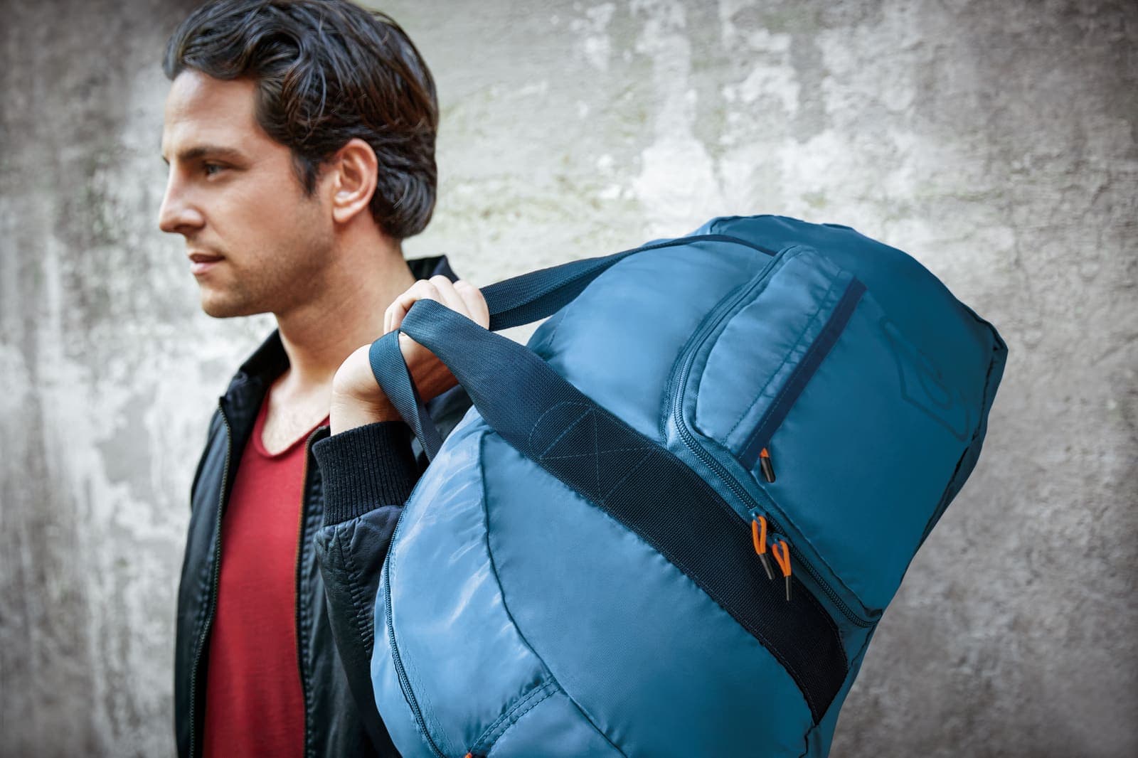 Man carrying a blue GO TRAVEL foldaway travel bag.