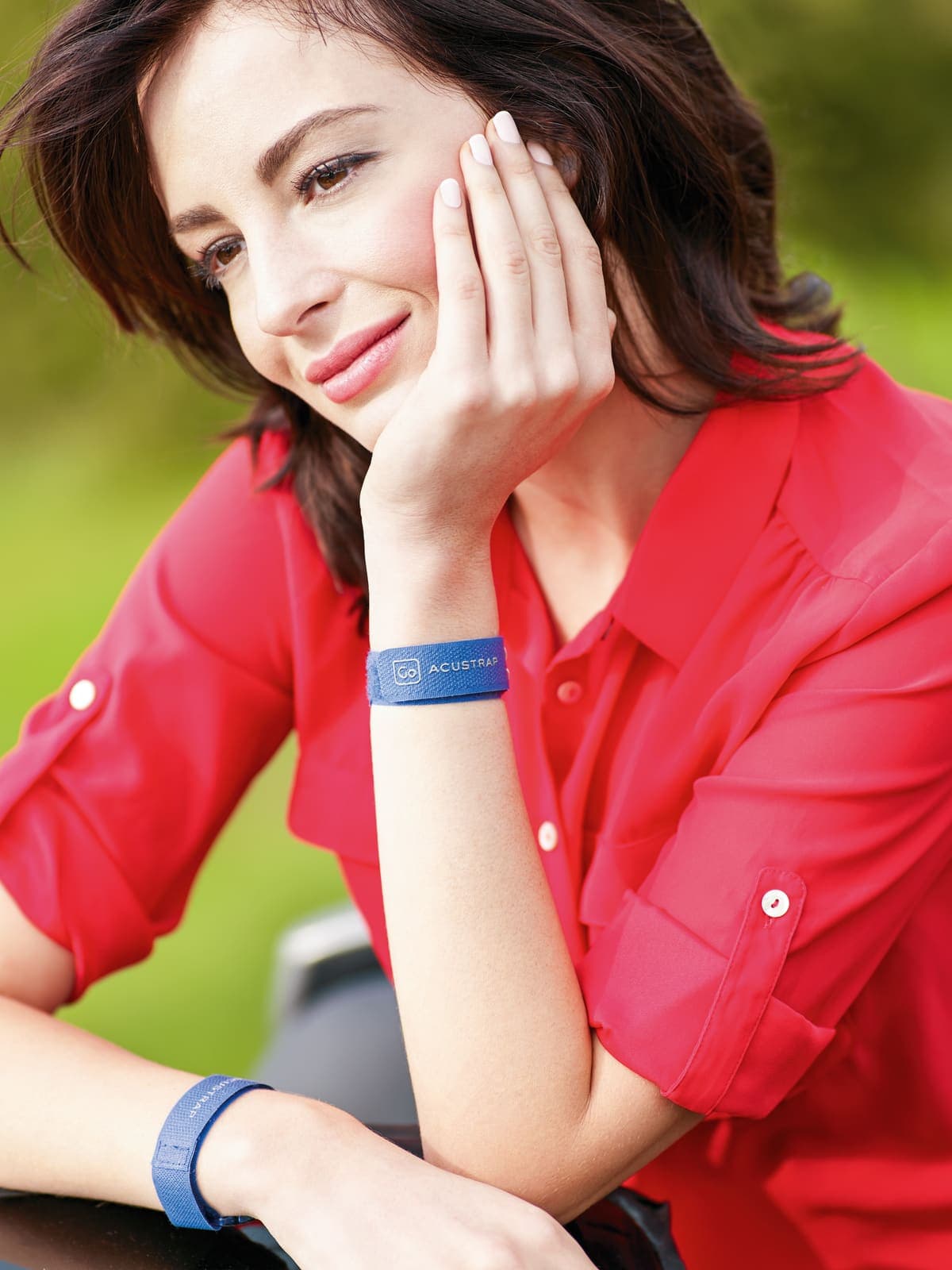 Woman wearing a blue Acustraps motion sickness band on her wrist, smiling outdoors.