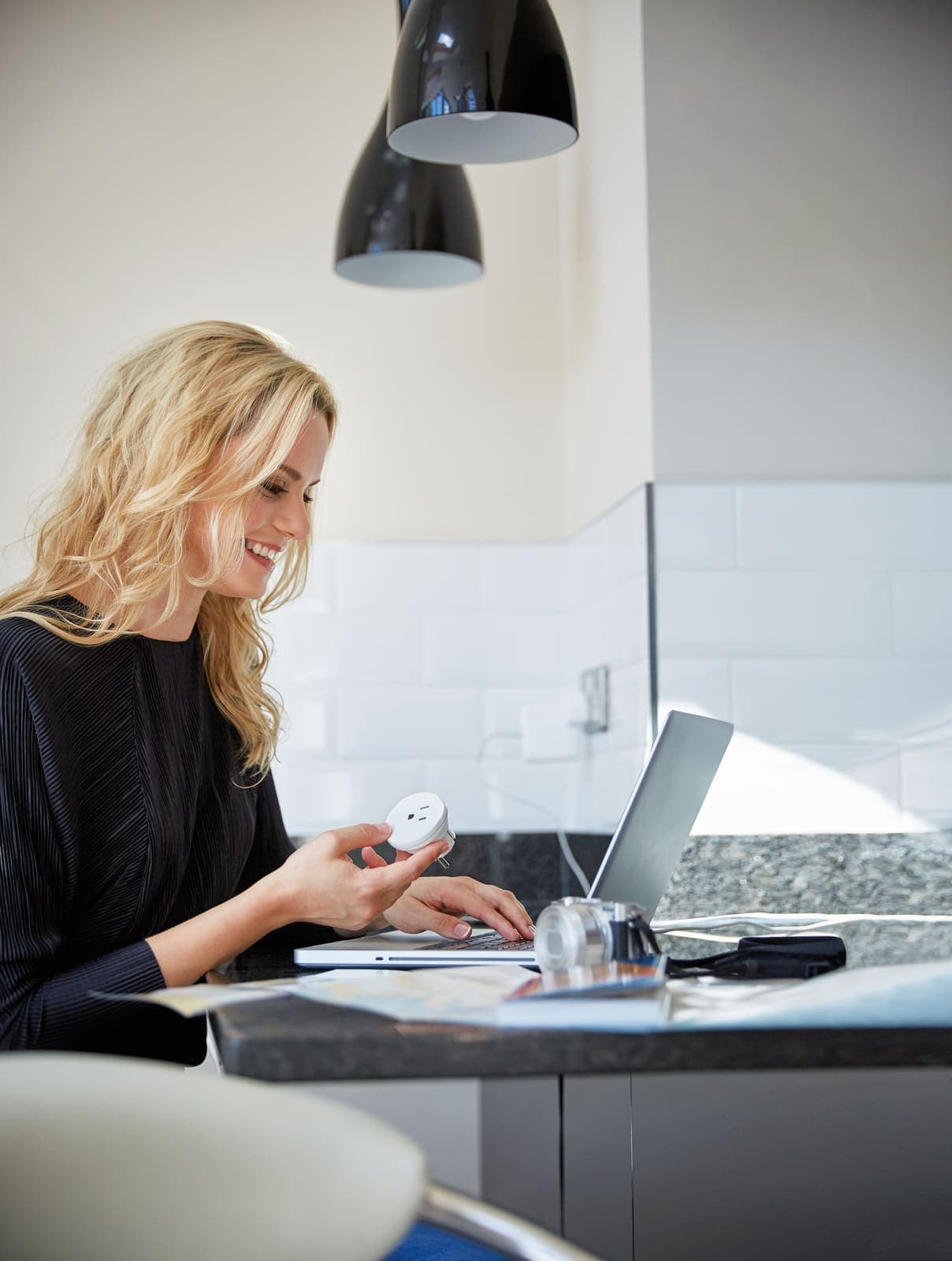 Woman holding a GO TRAVEL USA-EU adaptor while using a laptop.