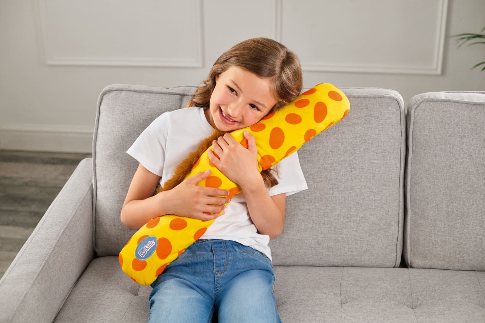 Girl hugging a yellow giraffe travel pillow on a sofa.