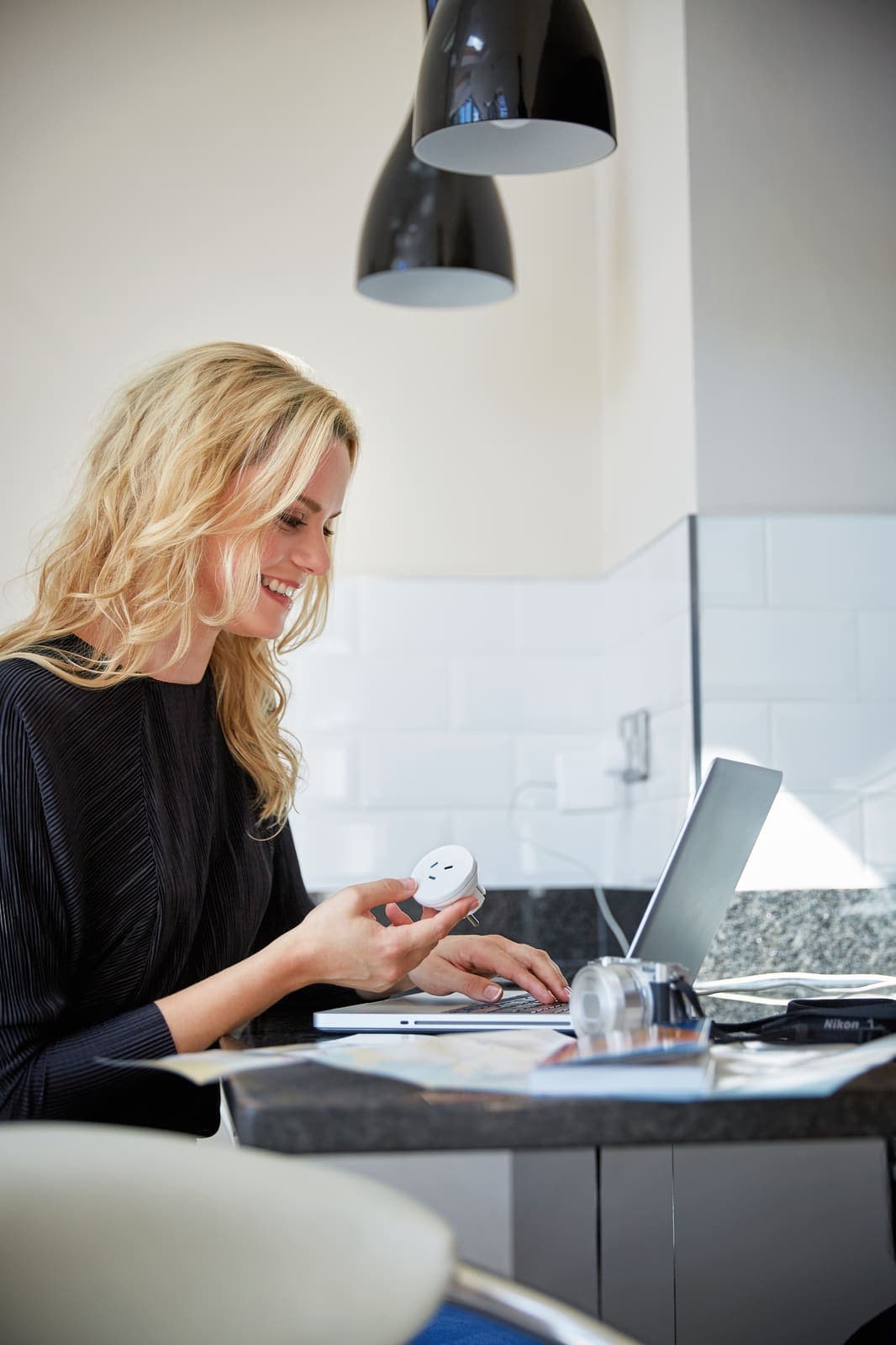 Woman with GO TRAVEL AUS/China-EU adaptor and laptop in a kitchen.