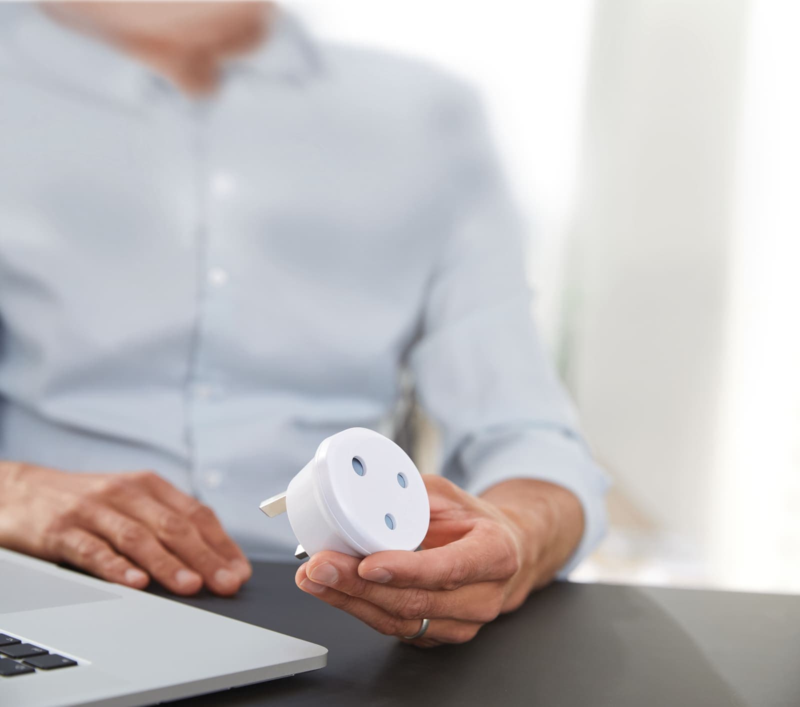 Person holding a white travel adapter next to a laptop.