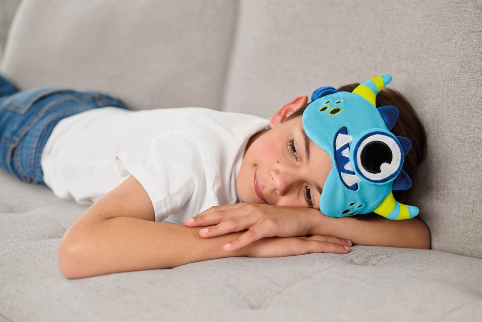 Boy wearing a blue monster eye mask while resting on a couch.