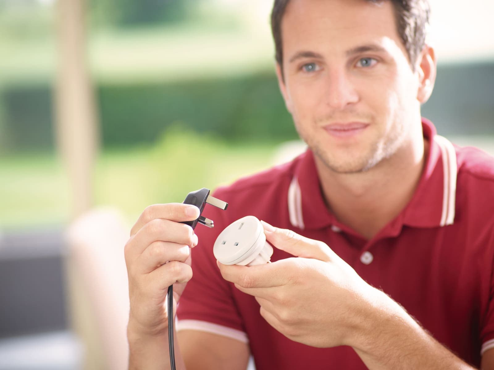 Man holding a white GO TRAVEL UK-EU adapter and a black UK plug outdoors.
