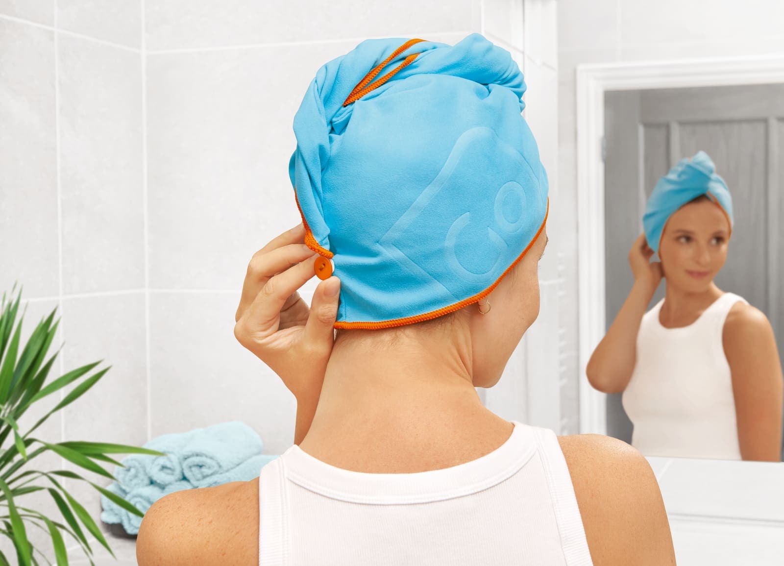 Woman in bathroom securing a blue quick-drying hair wrap with orange trim.